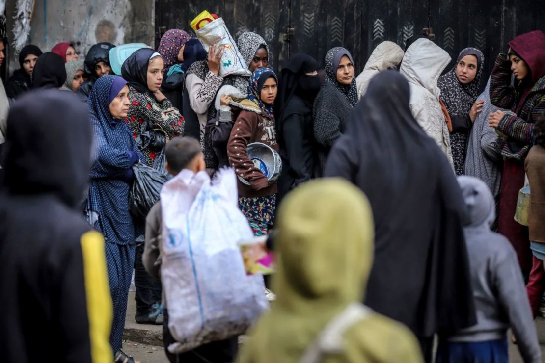 Palestinos hacen fila con contenedores para recibir comidas gratuitas en un campamento temporal en Deir al-Balah, en el centro de Gaza.