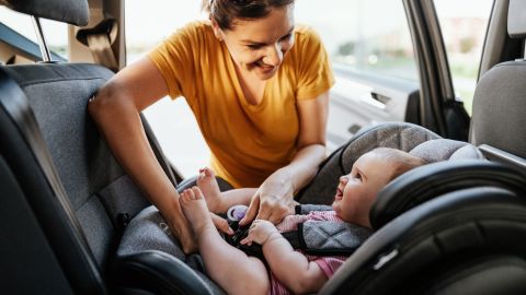 A photo of a person putting a baby in a rear-facing car seat.