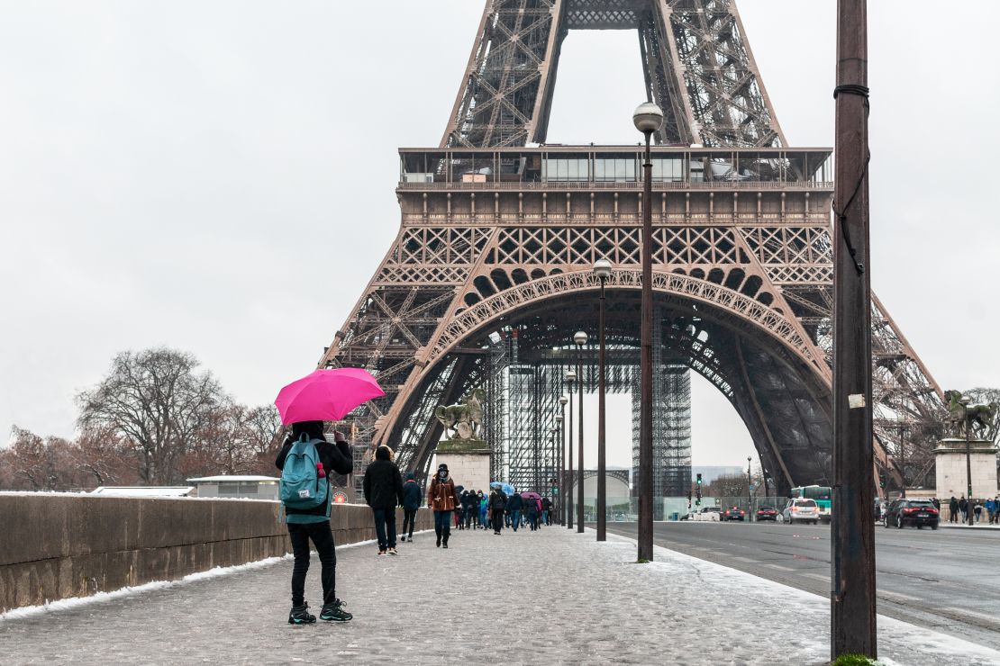 A photo of a person holding a pink umbrella in front of the Eiffel Tower in Paris, France on a gloomy day