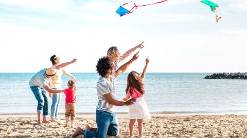 A photo of two families with small children flying kites on the beach