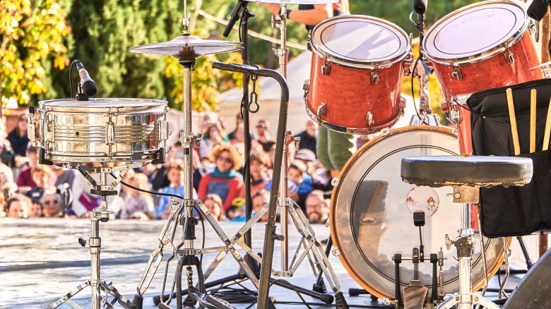 A photo of a drumset on a stage at an outdoor music festival with music fans in the background