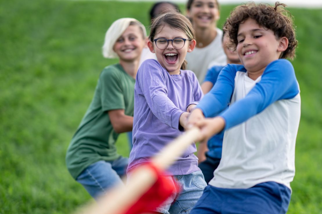 A small group of school aged children pull a rope with all their might, as they participate in a game of tug-of-war. They are each dressed casually and are smiling and laughing as they pull together.