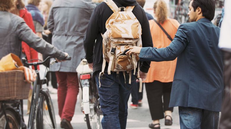 A photo of a person taking a wallet out of another person's backpack on a crowded street