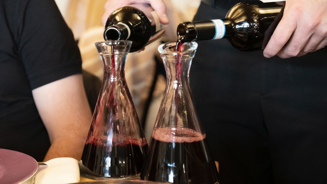 Two bottles of wine being poured into a decanter