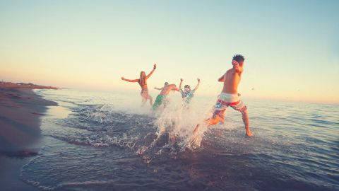 A photo of a group of people running from a beach into a body of water