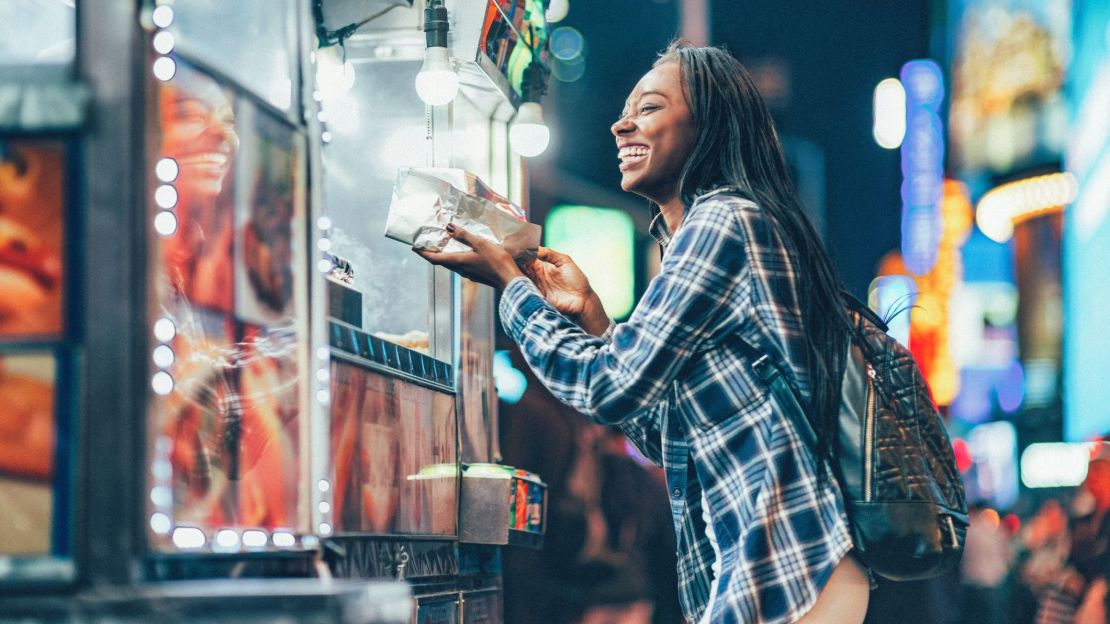 A photo of a person buying food from a food cart in New York City at night