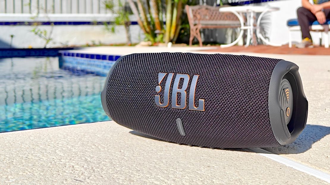 The JBL Charge 5 Wi-Fi speaker on a ground next to a swimming pool.