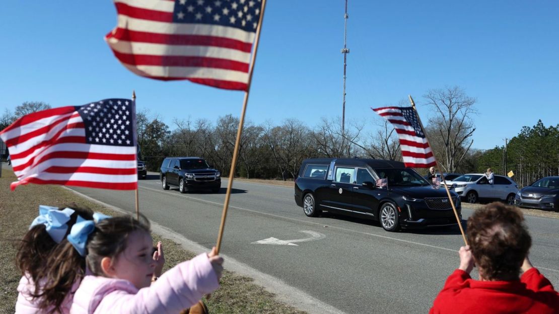 Niños agitan banderas mientras el auto fúnebre de Carter pasa este sábado en Plains.