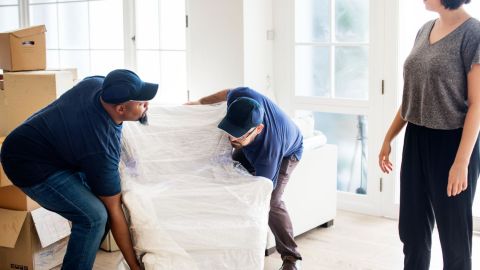 Two movers picking up a chair wrapped in plastic.