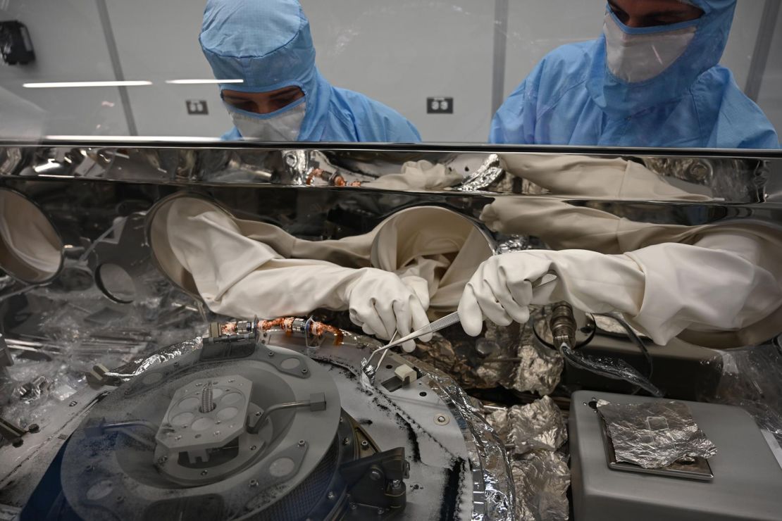 Die Astronomie-Materialbearbeiter Mary Montoya (links) und Curtis Calva sammeln mithilfe von Instrumenten Asteroidenpartikel von der Basis des OSIRIS-REx-Wissenschaftsgeheges.