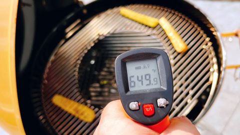 An infrared thermometer measuring the surface temperature of a Weber Kettle grill.