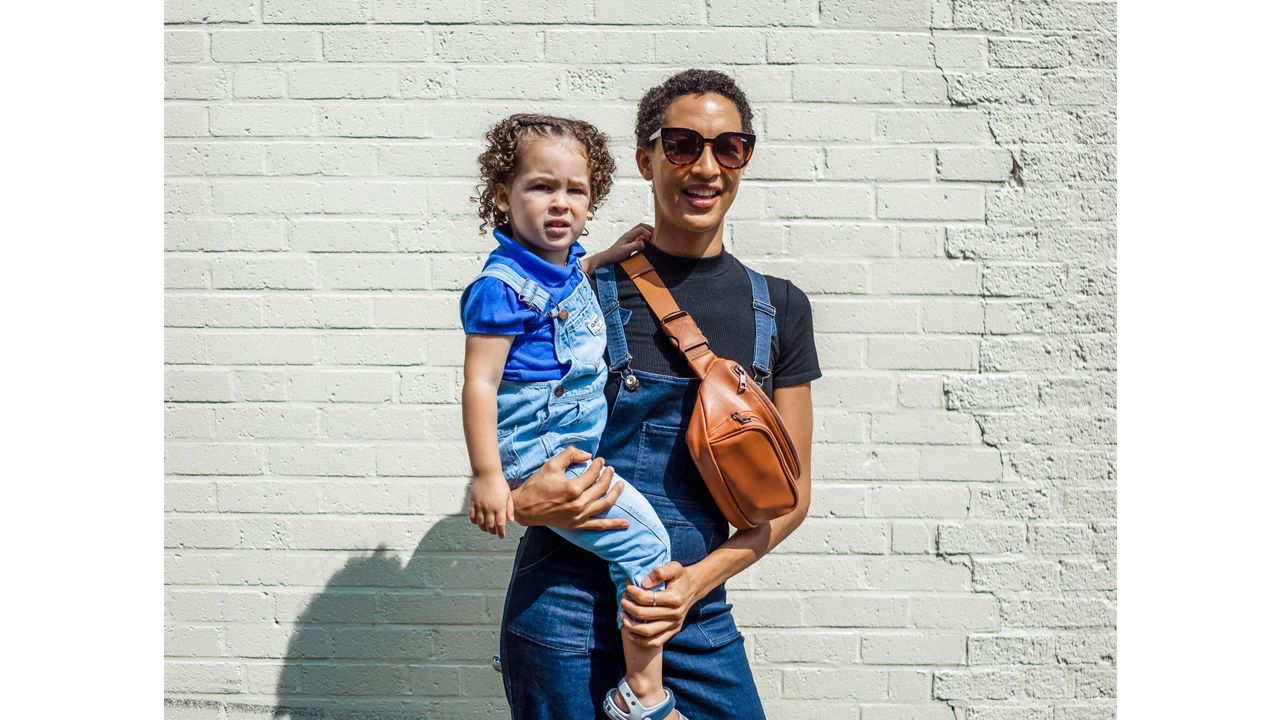 A photo of a person carrying a child with the Kibou Vegan Leather Diaper Bag around their shoulder