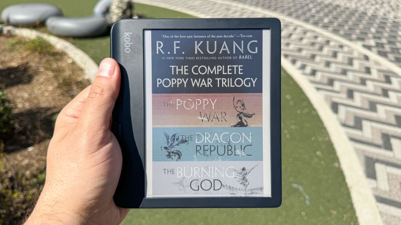 The Kobo Libra Colour e-reader used outside, open to the cover of R.F. Kuang’s “The Complete Poppy War Trilogy,” which renders in color with reddish orange and blue hues in addition to black and white.