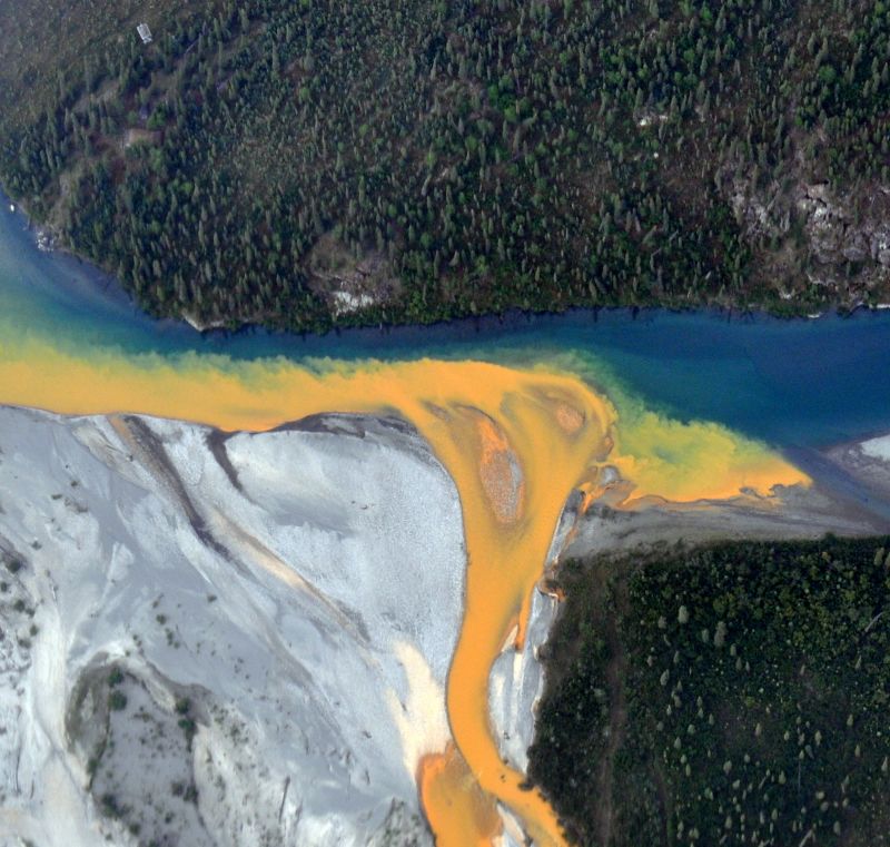 An aerial view of the Kutuk River in Alaska's Gates of the Arctic National Park that looks likeorange paint spilling into the clear blue water.