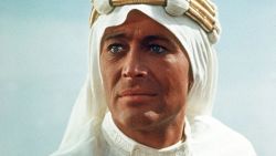 Close-up of Peter O'Toole as T.E. Lawrence in "Lawrence of Arabia." He's looking slightly off to the left, dressed in the character's signature white desert garb, including head covering, against a light blue sky.