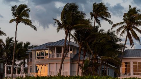 Hurricane winds blow palm trees outside a coastal home.