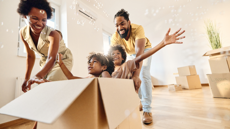 Parents having fun while pushing their small kids in a cardboard box at new home