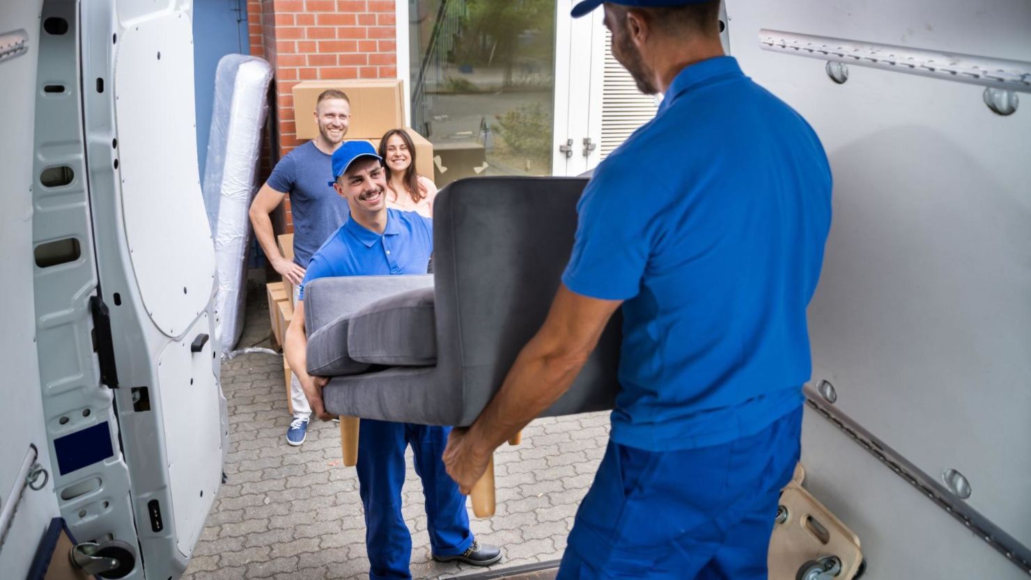 Two movers lift a couch from a moving van.