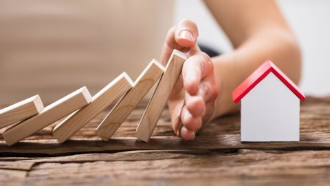 Human hand stopping blocks from falling on a model house.