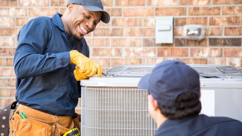 Two air conditioner repair workers fixing an AC system.