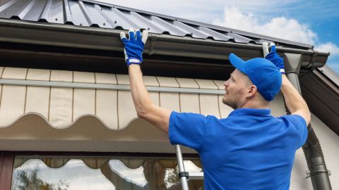 Gutter guard installer puts a gutter guard on the side of a house.