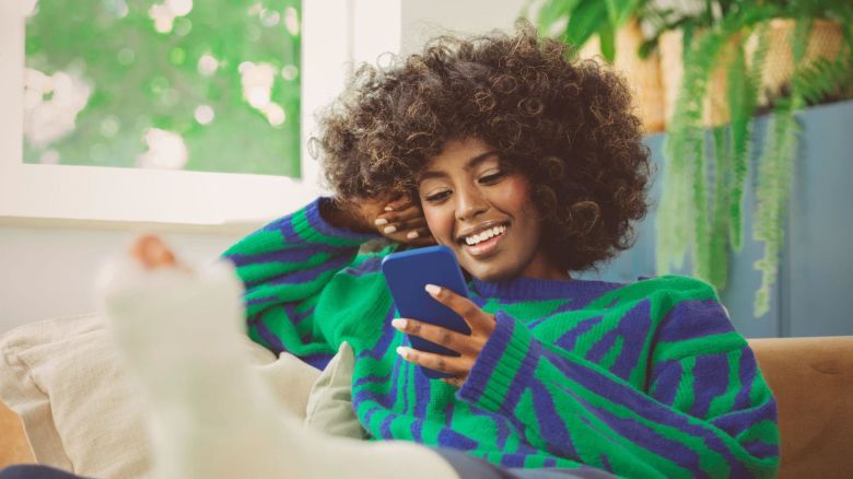 Young adult with a broken leg using a mobile phone in their apartment.