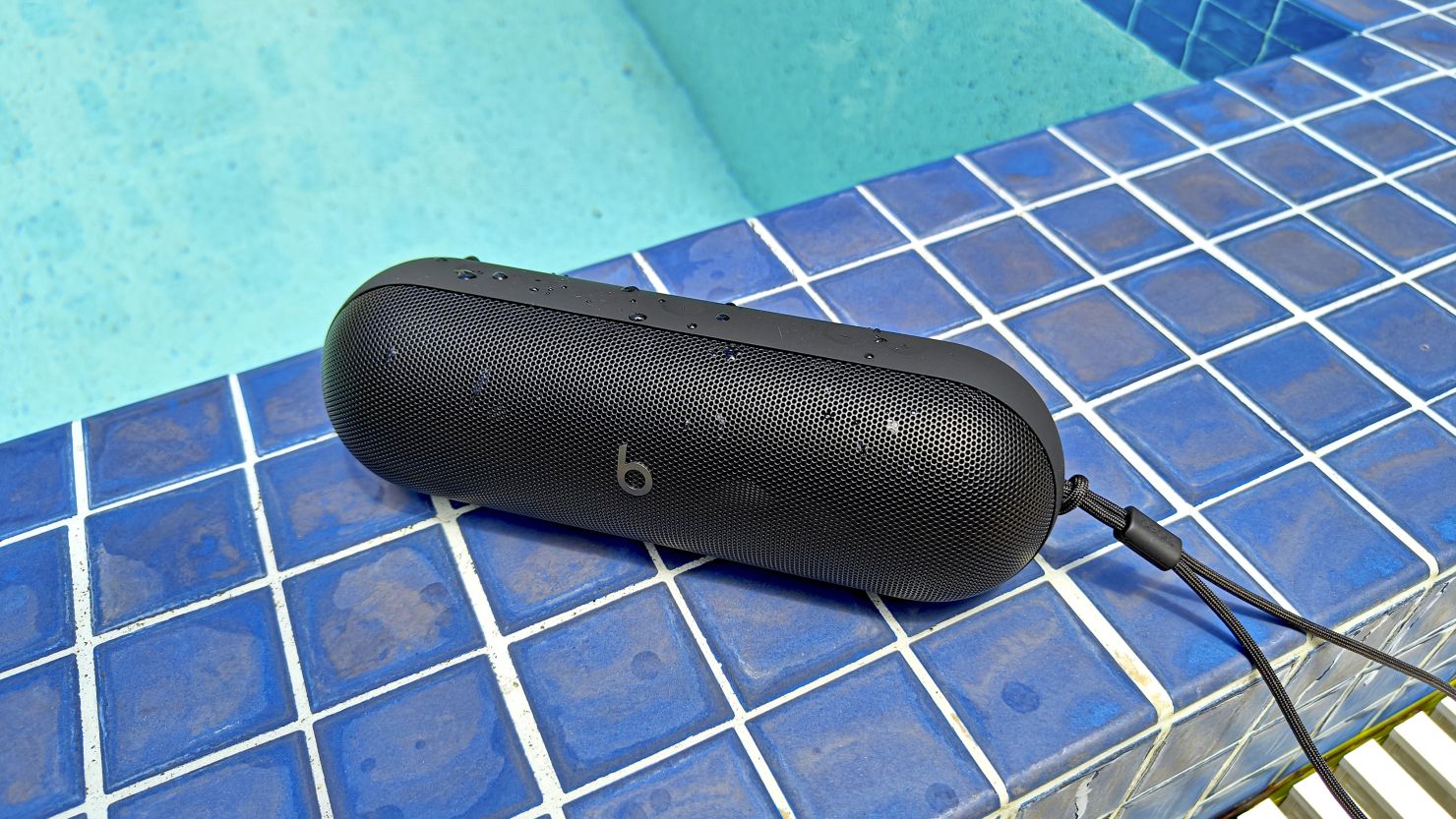 A black Beats Pill speaker at the edge of a swimming pool.