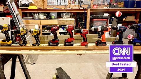 Nine drills lined up on a table in a workshop.