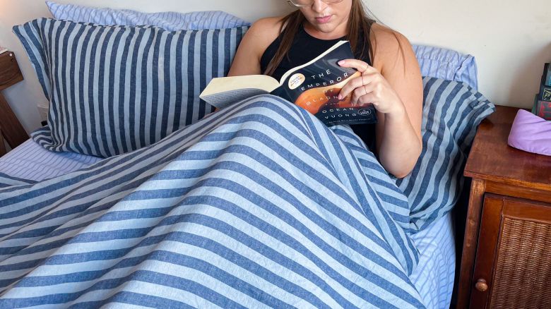Person reading on a bed with one of our best recommended comforters for hot sleepers.