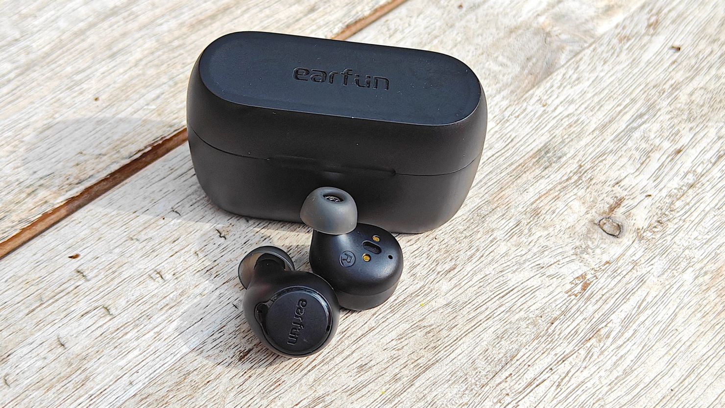 The EarFun Free 2S earbuds and their case on a wooden surface.