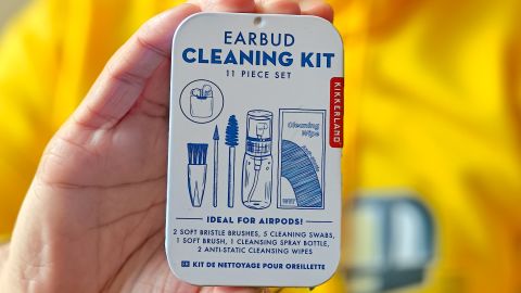 An earbud cleaning kit held in front of a person wearing a yellow shirt.