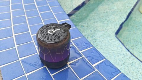 Anker Soundcore Glow Mini speaker next to a pool with splashes of water on it.