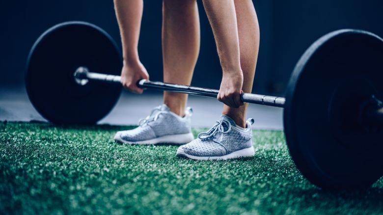 Fit caucasian Girl picking up heavy barbell with weights for workout