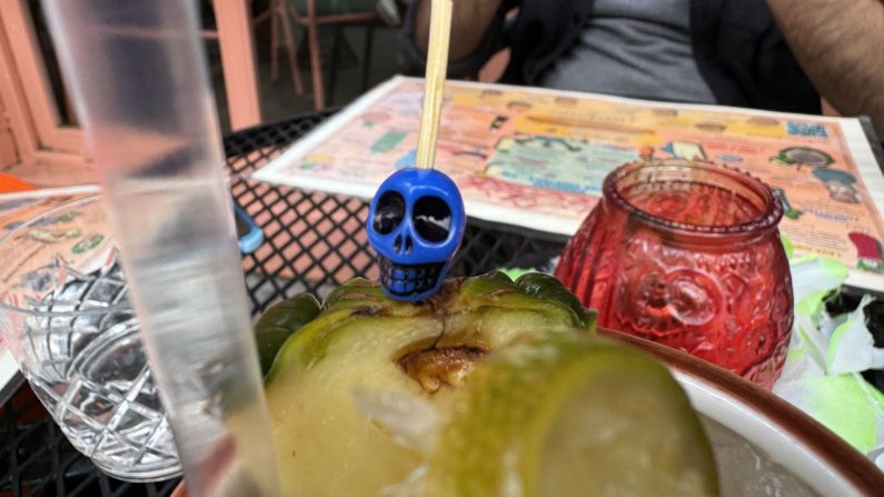 a blue skull is attached to the top of a pineapple wedge in a drink, but it's not as much in focus