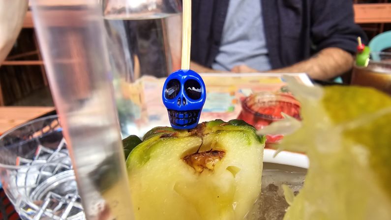 a blue skull is attached to the top of a pineapple wedge in a drink