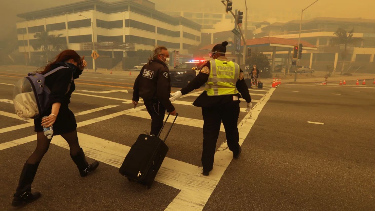 Un evacuado recibe ayuda para cruzar el Pacific Coast Highway mientras el humo del incendio Palisades envuelve Sunset Boulevard el martes.