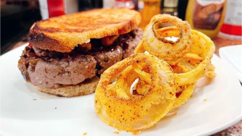 A steak sandwich and onion rings, prepared in a carbon steel pan.