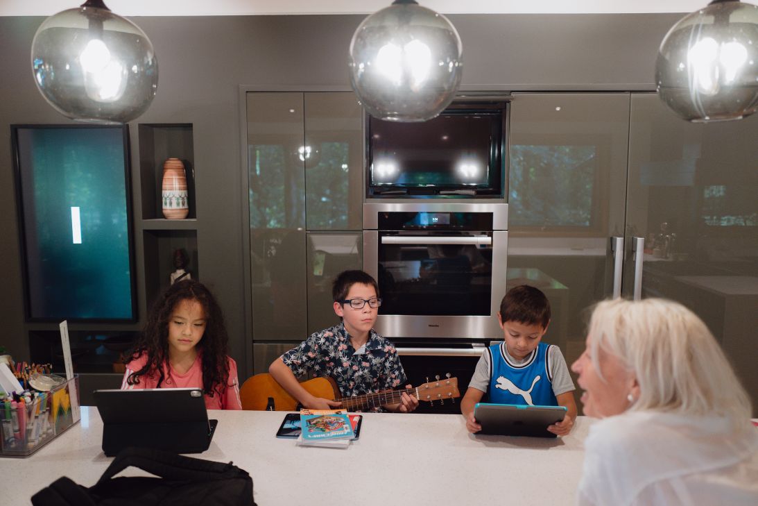 Carlos practices guitar while his siblings play on their tablets.