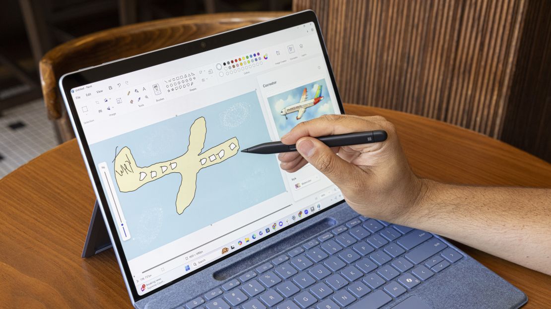 一只手在 Microsoft Surface Pro 2024 上的 Paint 应用程序中绘制了一架飞机，旁边是 AI 生成的版本。