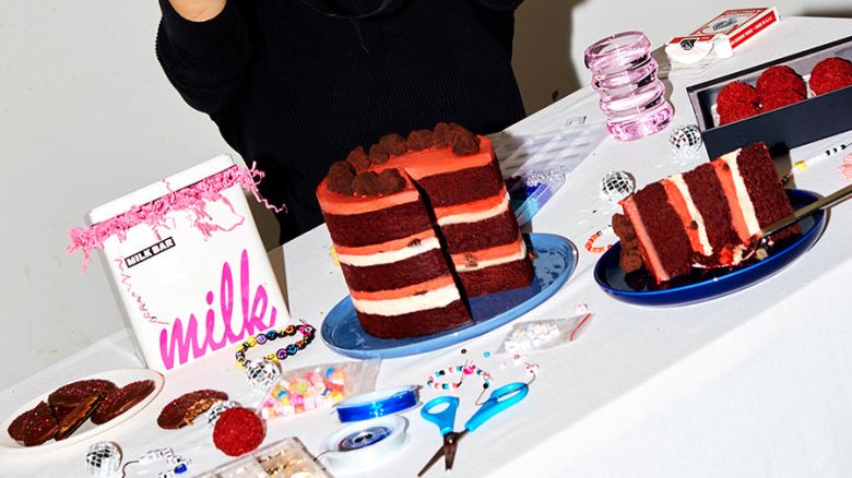 A cut cake and several party materials on a white table with a person standing behind it.