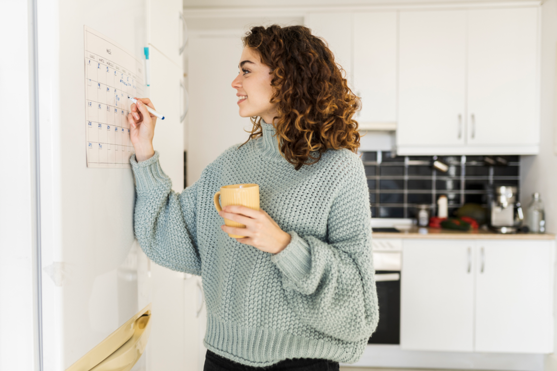 Woman writes on a calendar in the kitchen.