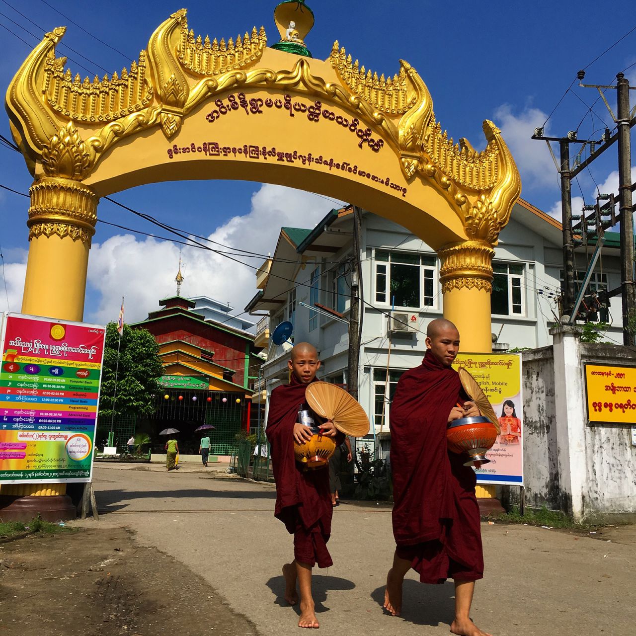 Monks head out to collect alms from Insein Ywama Monastery near Yangon. Behind them are posters offering English and computing classes.