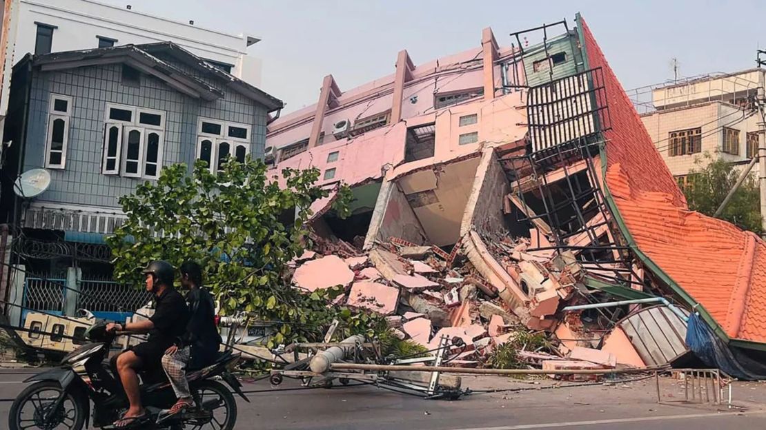 Personas pasan en moto por delante de un edificio derrumbado en Mandalay el 28 de marzo de 2025, tras el terremoto en el centro de Myanmar.