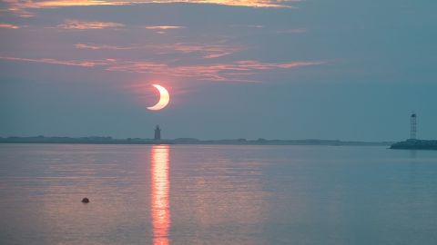 A partial solar eclipse is seen as the Sun rises behind the Delaware Breakwater Lighthouse on June 10, 2021, at Lewes Beach in Delaware.
