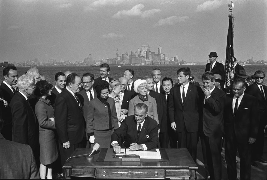 President Lyndon B. Johnson signs the Immigration and NationalityAct of 1965 as Vice President Hubert Humphrey, Lady Bird Johnson, Muriel Humphrey, Sen. Edward (Ted) Kennedy, Sen. Robert F. Kennedy, and others look on. October 3, 1965.
