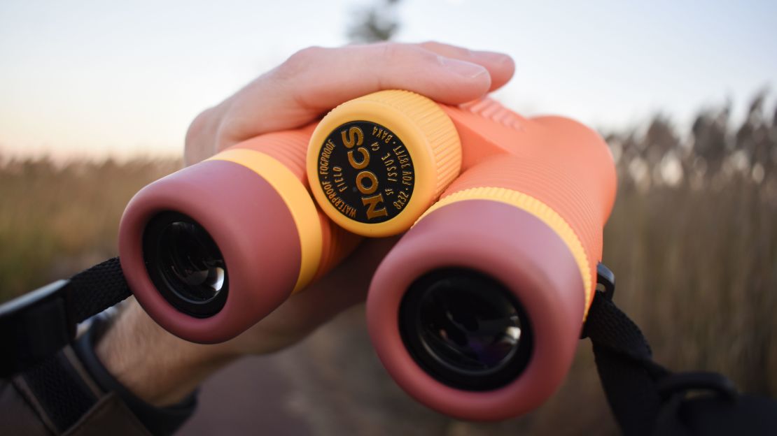 Orange binoculars gripped by someone's left hand.