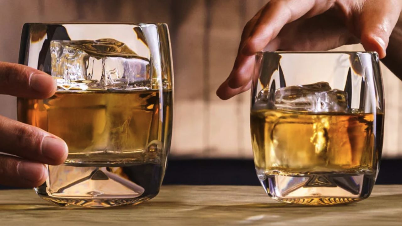 Two Norlan Rauk Heavy Tumblers filled with ice and whiskey. Each is held in a different person's hand.