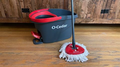 The O-Cedar EasyWring Microfiber Spin Mop with bucket, seen on a hardwood floor standing in front of a wooden cabinet.