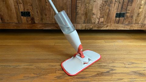 The OXO Good Grips Microfiber Spray Mop seen on a hardwood floor in front of a wooden cabinet.