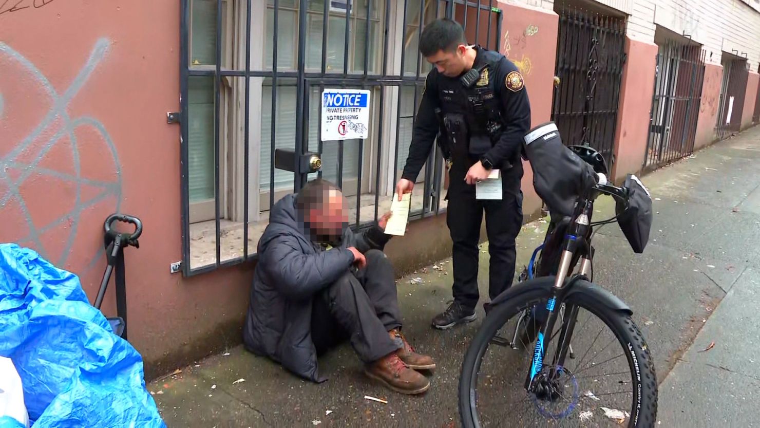 A Portland, Oregon, police officer issues a citation and treatment card to a man using fentanyl in public; CNN has blurred this image to protect the man's identity.